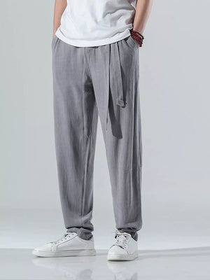 Men's grey relaxed fit casual pants with tie waist, styled with white sneakers.