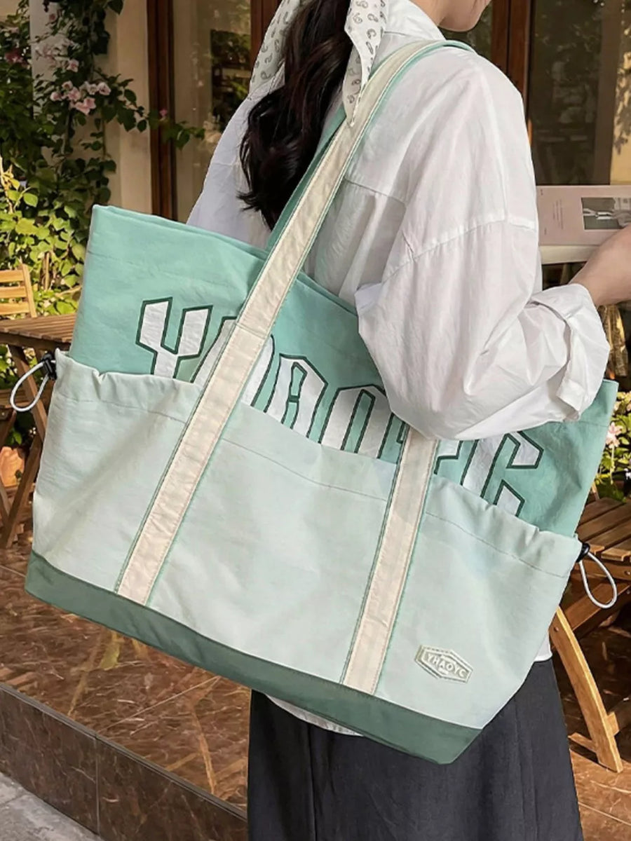Green drawstring shoulder bag with bold white lettering and side pockets.