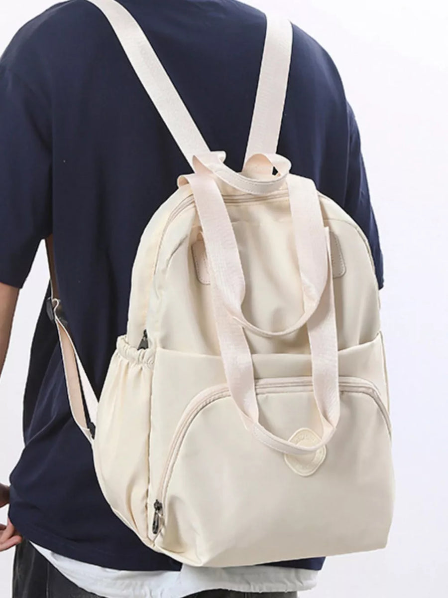 Off-white Oxford cloth backpack with adjustable straps and multiple pockets.