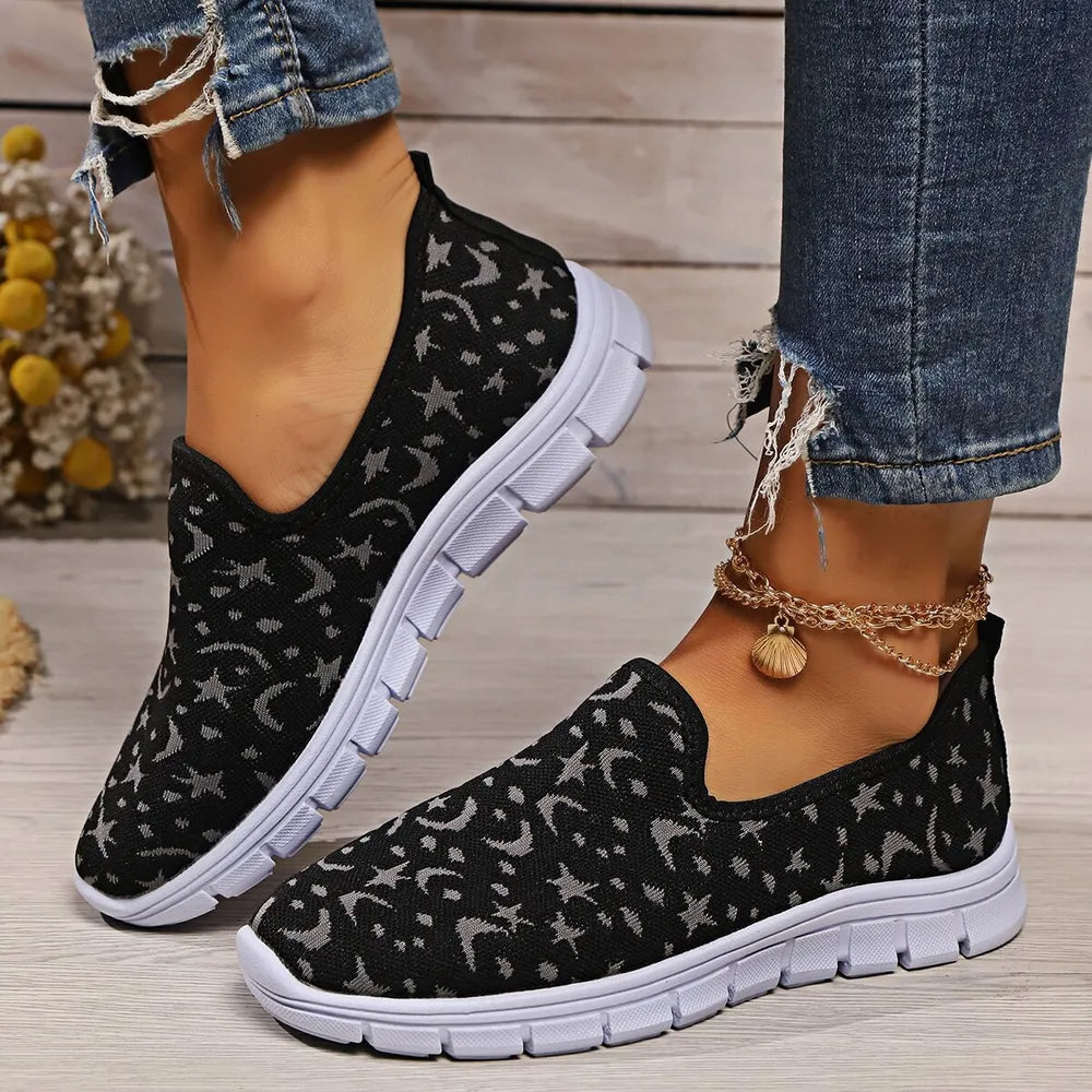 Black knit slip-on sneakers with a celestial star and moon pattern and white soles.