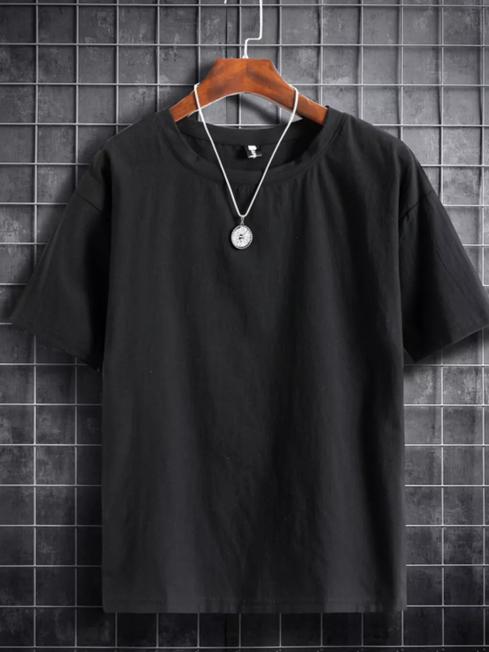 Black cotton crew neck t-shirt with short sleeves and a simple pendant necklace.