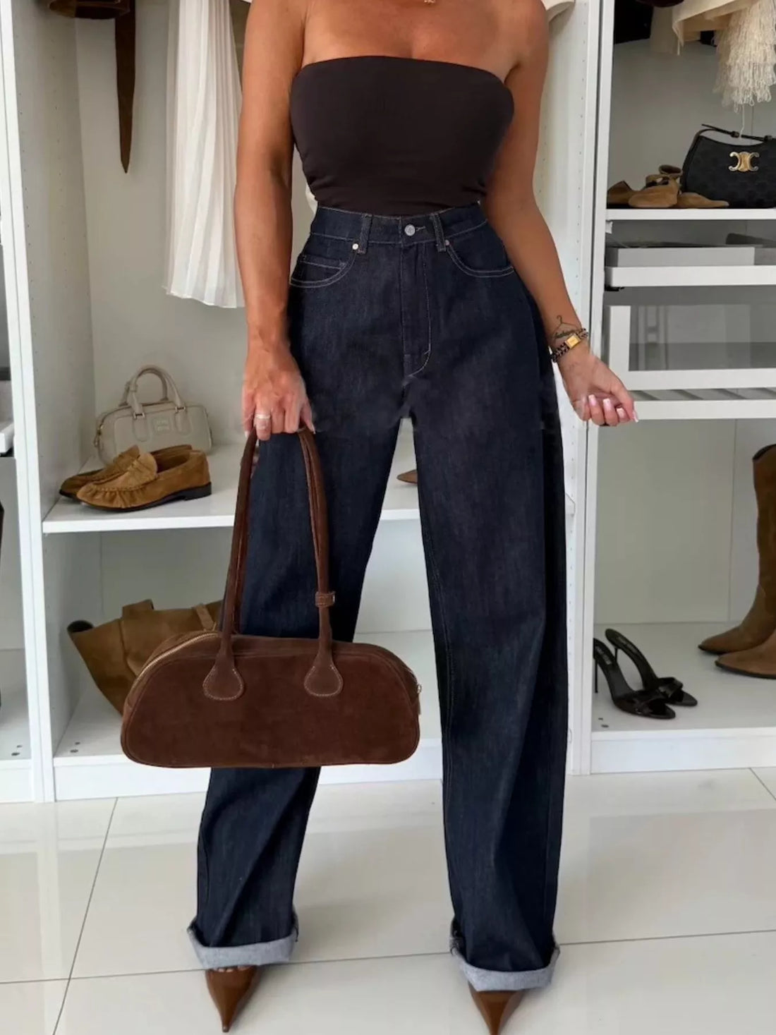 High-waisted wide-leg jeans in dark navy denim with a cuffed hem, styled with a tube top and brown suede handbag.