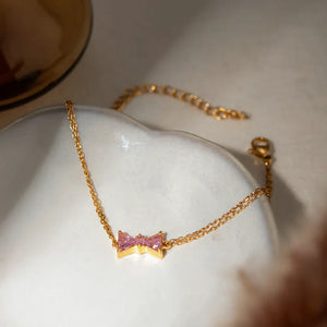 Gold chain bracelet with pink gemstone bow detail
