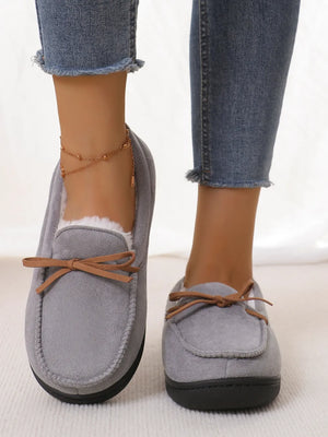 Gray suede moccasin slippers with white faux fur lining and brown bow detail.