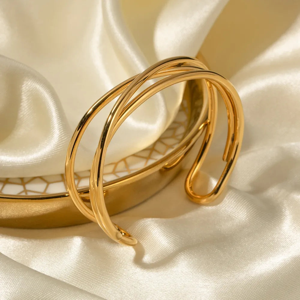 Gold-tone open cuff bracelet with intertwined design on satin fabric.
