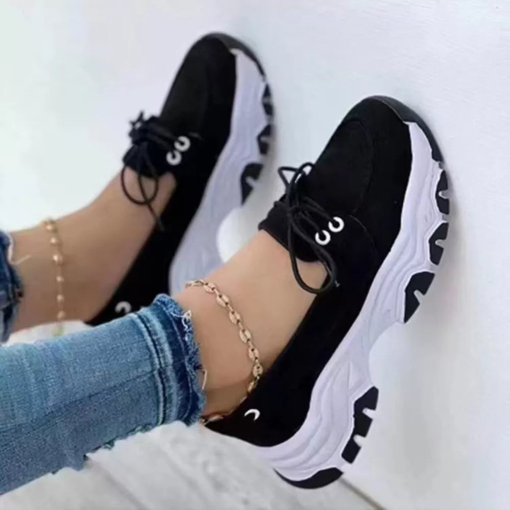 Black lace-up sneakers with white chunky soles and round toes.