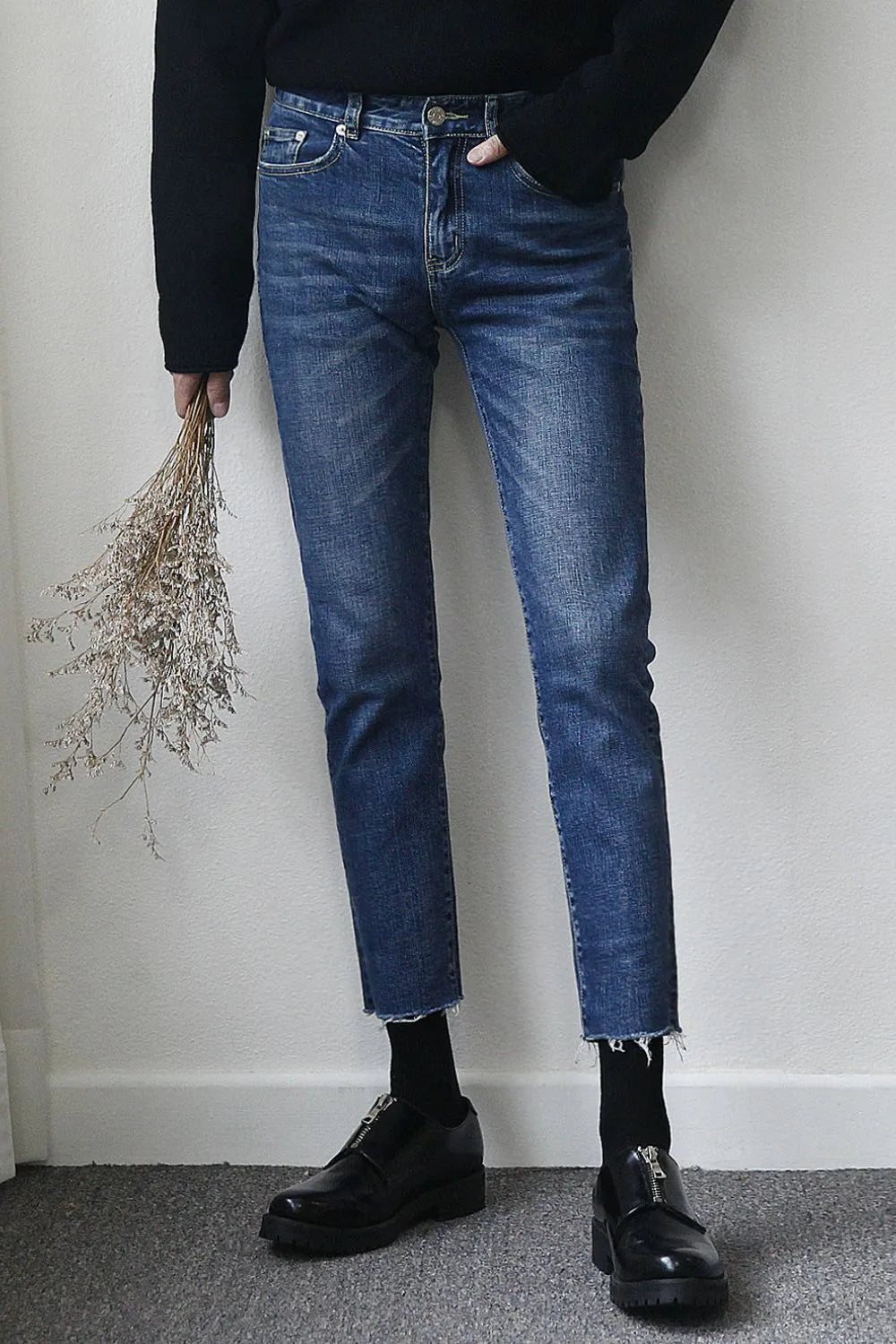 Medium wash slim-fit jeans with raw hem and distressed detailing.