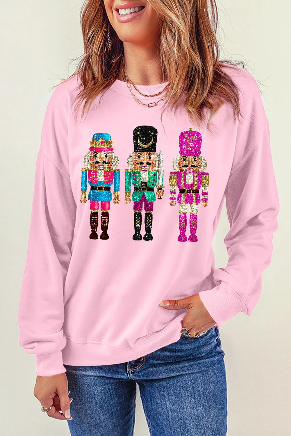 Blush pink crewneck sweatshirt with a graphic of three glittery nutcrackers.