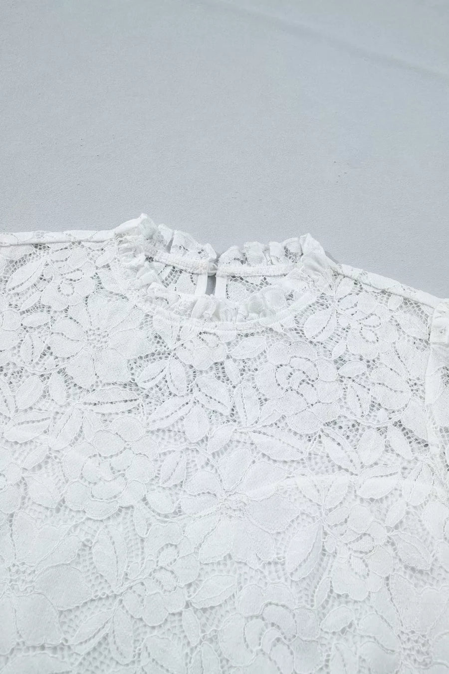 White lace blouse with ruffled mock neckline and floral pattern.