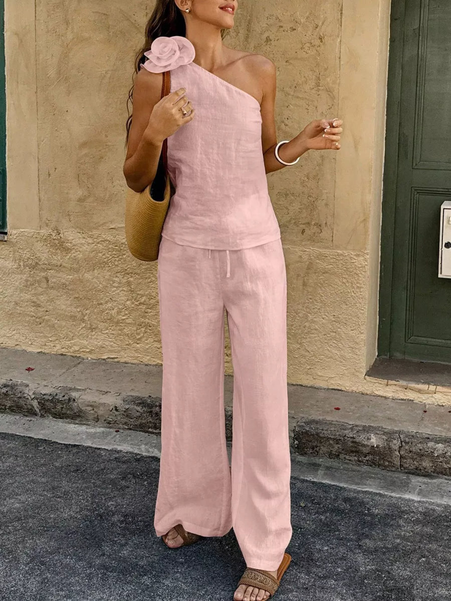 Pink cotton one-shoulder top with floral embellishment and wide-leg pants.