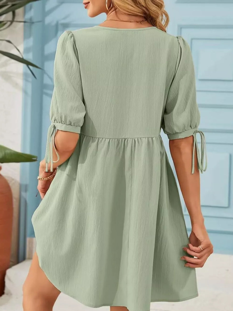 Light green mini dress with puff sleeves and tie details, tiered skirt.