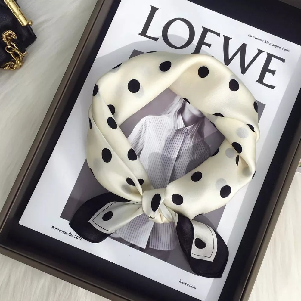 Cream white silk scarf with black polka dots and a bordered edge, tied in a knot.