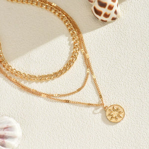 Gold layered necklace with chunky and delicate chains and a sunburst pendant.