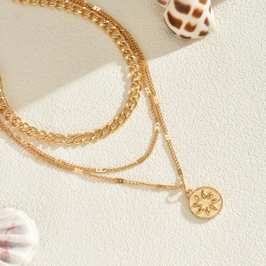 Gold layered necklace with chunky and delicate chains and a sunburst pendant.