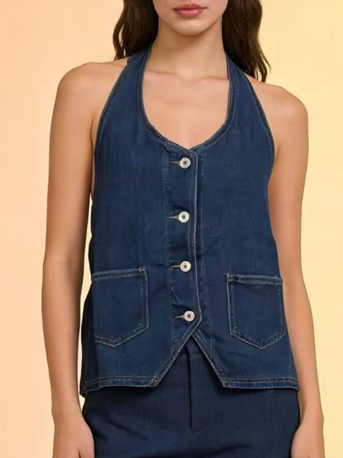 Button-down denim halter vest in dark blue with white buttons and chest pockets.