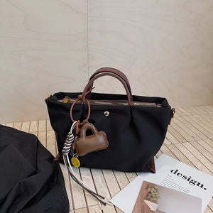Black compact nylon handbag with brown leather handles and charming bag keychain.