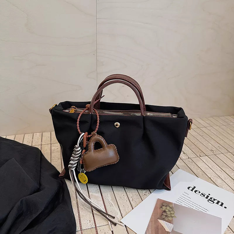 Black compact nylon handbag with brown leather handles and charming bag keychain.