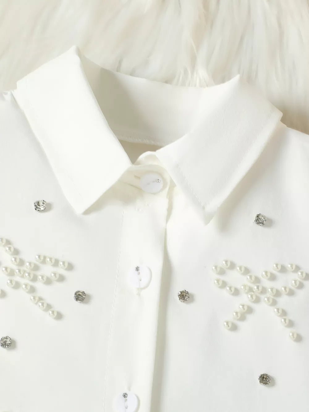 White baby girls' top with pearl bow and rhinestone embellishments.