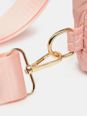 Glossy padded sling bag in pink with gold hardware and adjustable strap detail.