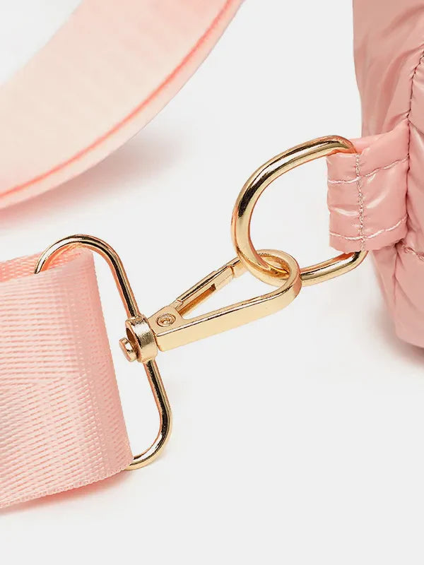 Glossy padded sling bag in pink with gold hardware and adjustable strap detail.