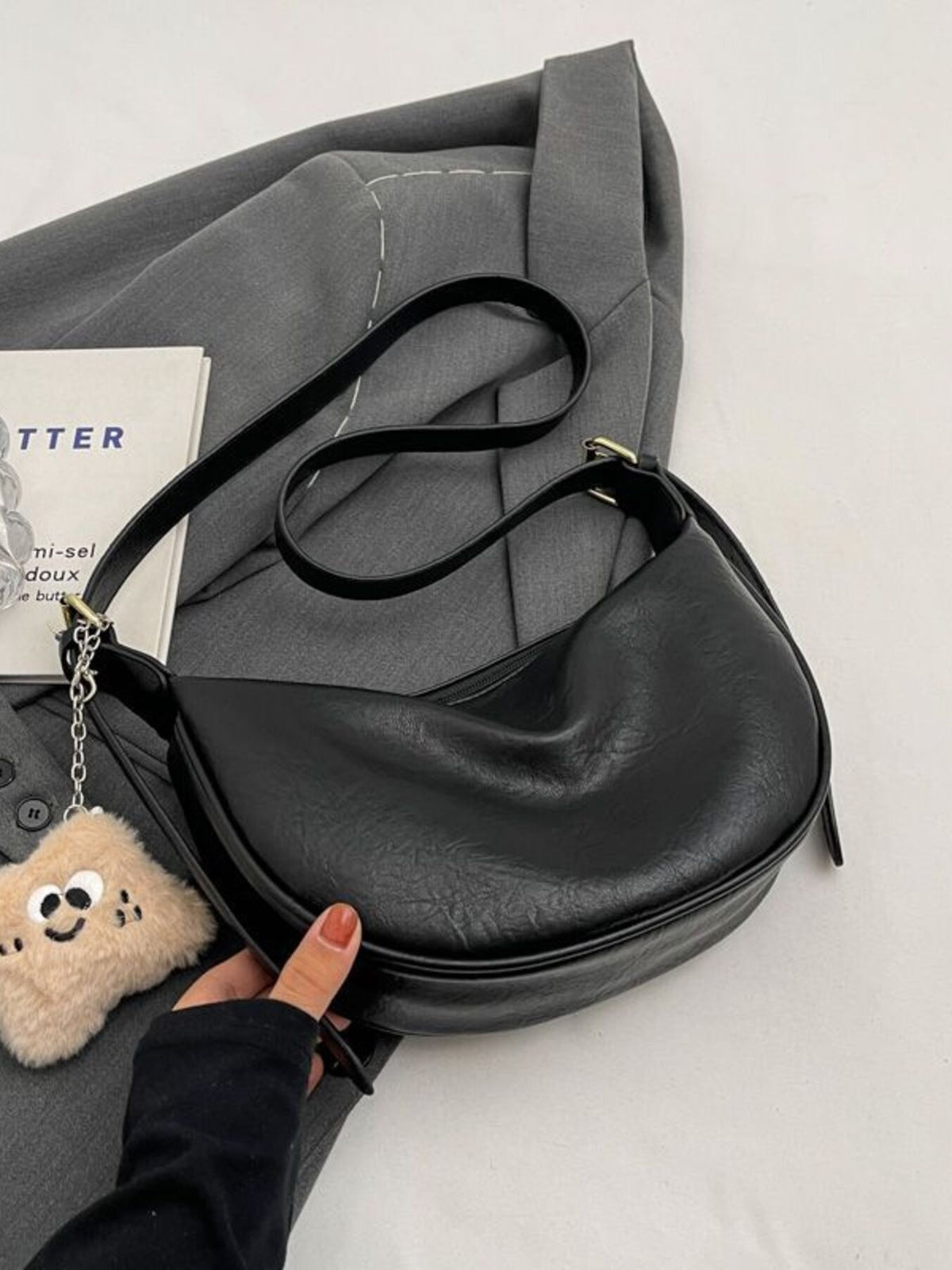Black crescent shoulder bag with plush charm and adjustable strap