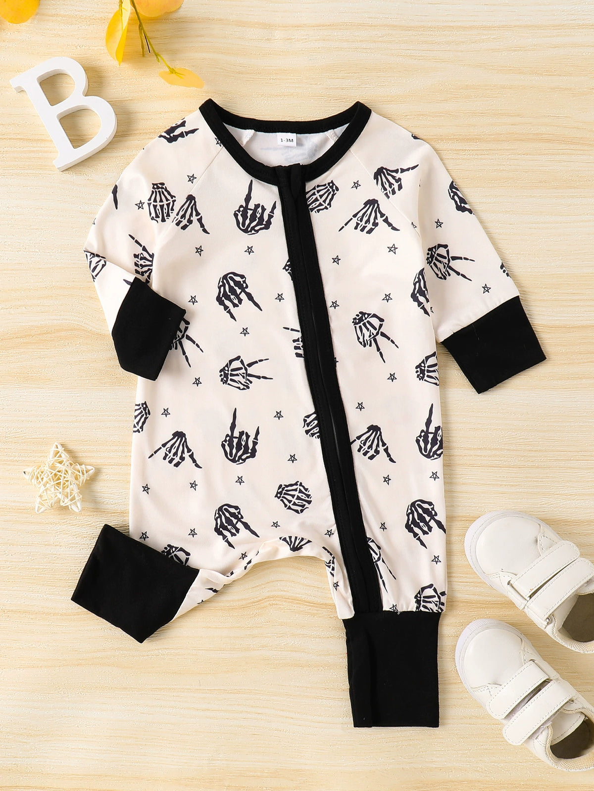 Beige baby one-piece with skeleton hand print, black trim and cuffs.