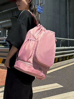 Blush pink drawstring duffle bag with zippered bottom compartment and side pockets.