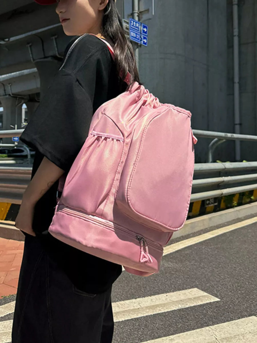 Blush pink drawstring duffle bag with zippered bottom compartment and side pockets.