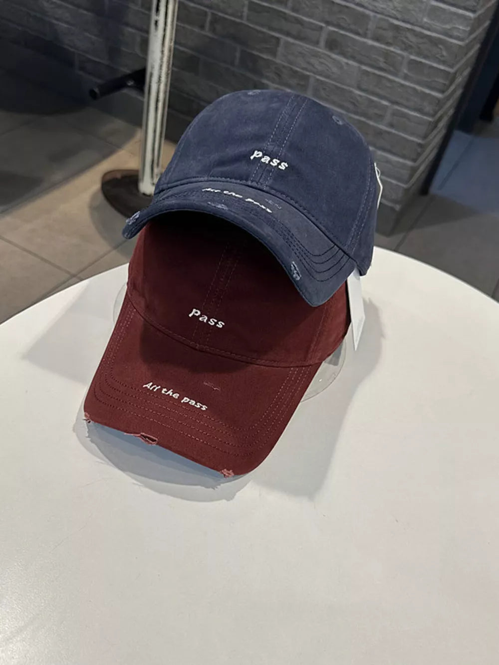 Distressed baseball caps in navy blue and wine red with embroidered slogans.