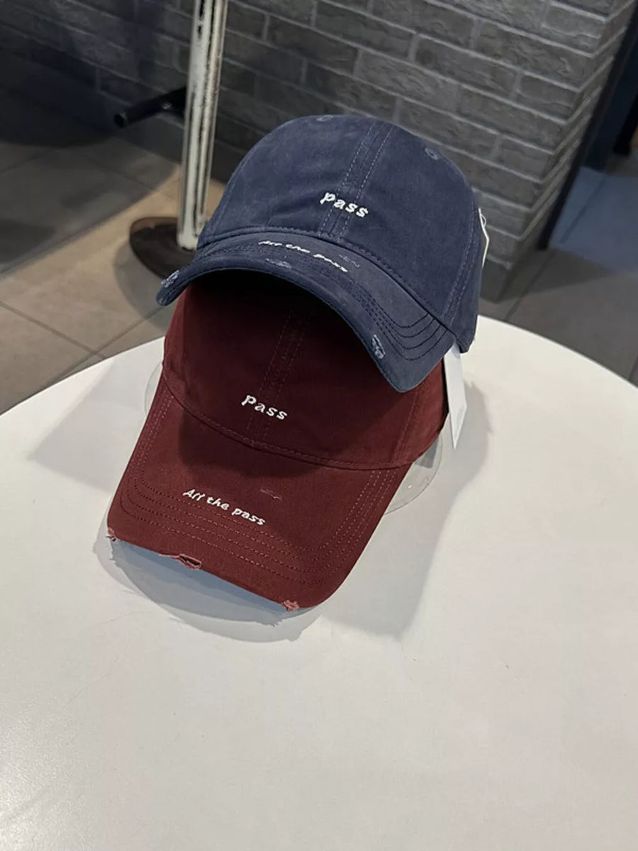 Distressed baseball caps in navy blue and wine red with embroidered slogans.