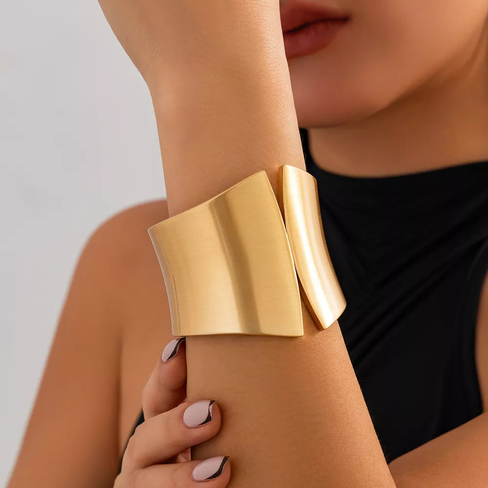 Gold-toned sculptural cuff bracelet with a wide, open design.