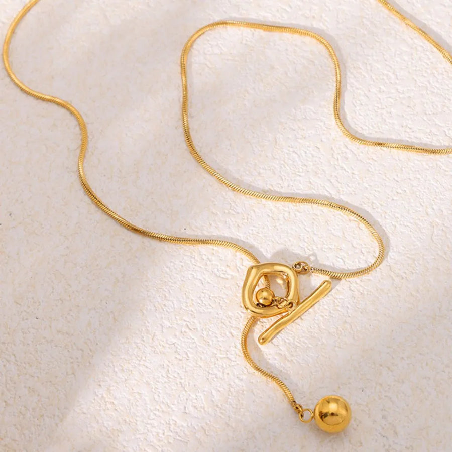 Gold lariat necklace with toggle closure and abstract square pendant.
