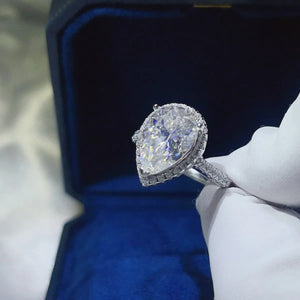 Pear-cut halo engagement ring in white metal with a large center stone and diamond-accented band.