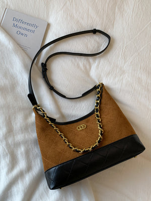 Brown half-moon crossbody bag with quilted black trim and gold chain detail