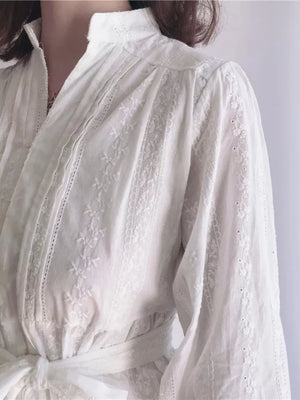 White cotton dress with embroidery and lace trim, featuring a high neckline and tie waist.