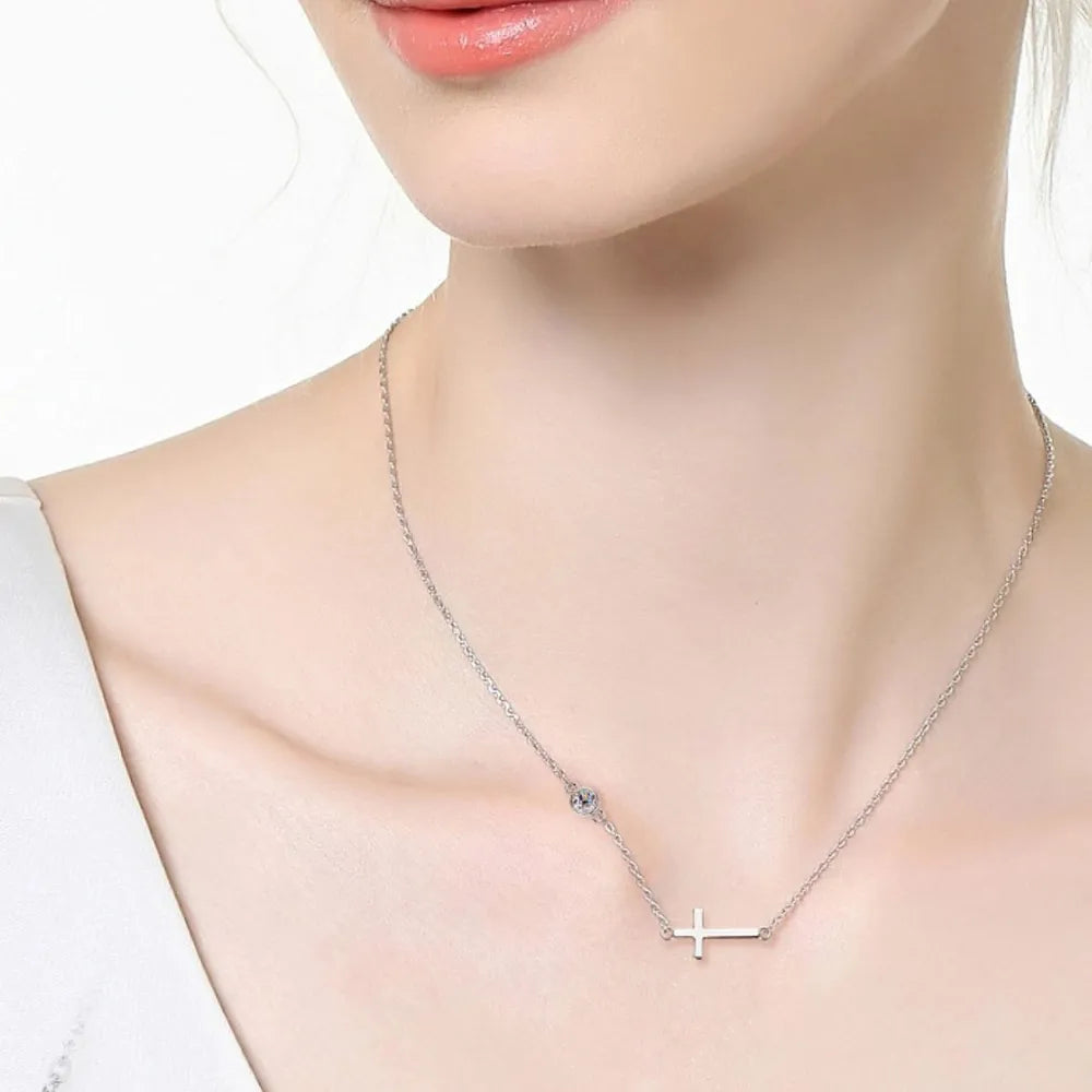 Silver asymmetrical cross pendant necklace with a delicate chain and single stone accent.