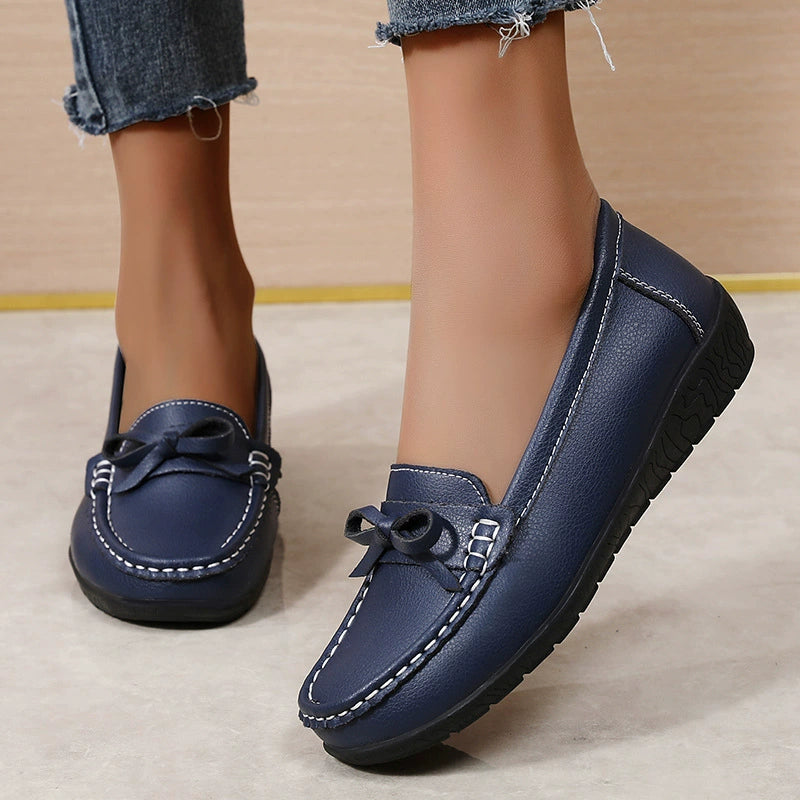 Dark blue slip-on loafers with bow detail and white stitching.