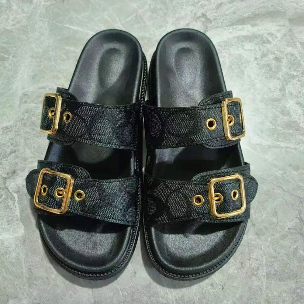 Black slide sandals with double buckle straps featuring a logo pattern and gold hardware.