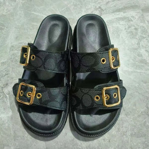Black slide sandals with double buckle straps featuring a logo pattern and gold hardware.