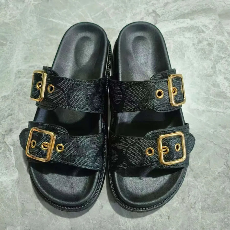 Black slide sandals with double buckle straps featuring a logo pattern and gold hardware.