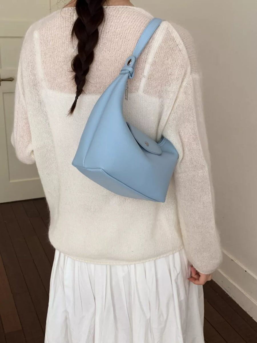 Blue crescent hobo bag with a flap closure and adjustable strap, worn crossbody.