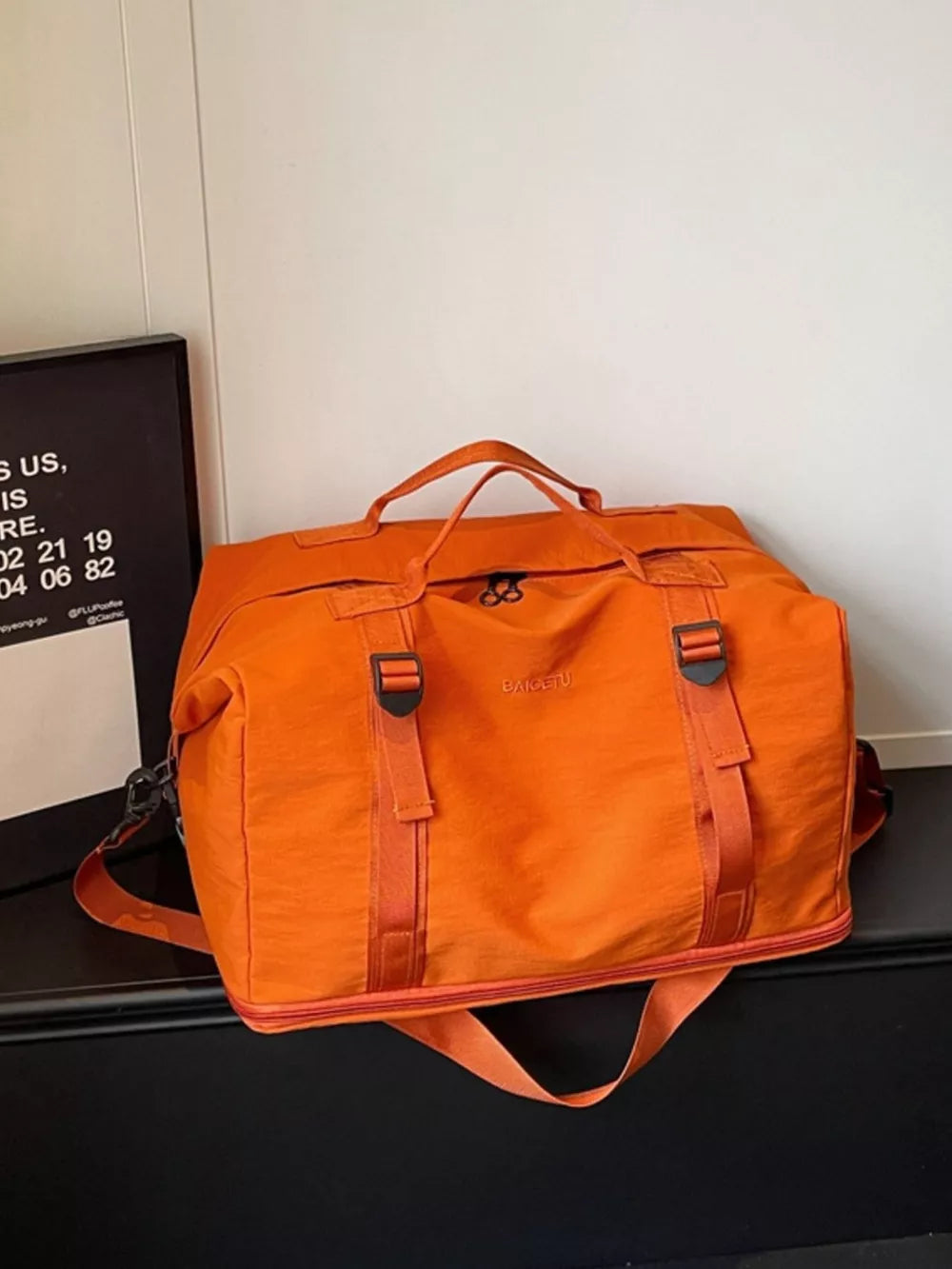 Orange nylon travel bag with buckle straps and adjustable shoulder strap.