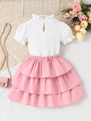 Toddler white ruffled mock neck top with puff sleeves and pink tiered skirt with elastic waistband.