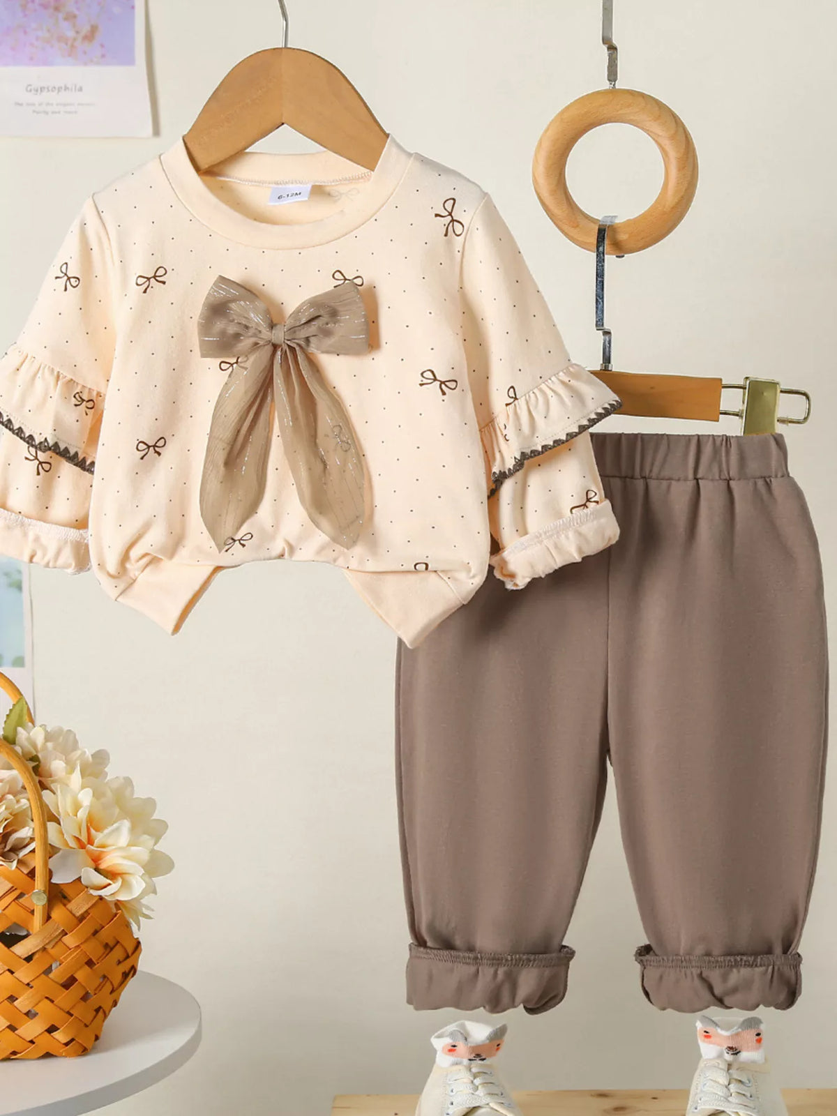 Tan baby outfit with ruffle sleeve top featuring bow print and large bow detail, paired with matching pants.