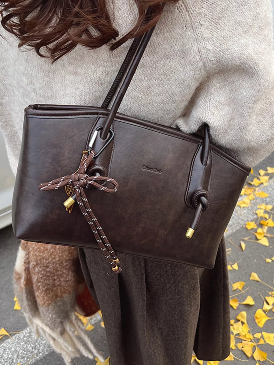 Brown leather shoulder bag with decorative knot and charm detail