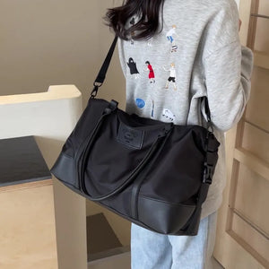 Black duffel bag with leather accents and adjustable strap, worn crossbody.