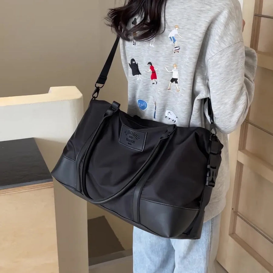 Black duffel bag with leather accents and adjustable strap, worn crossbody.