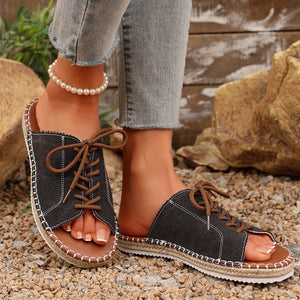 Black lace-up open-toe flat sandals with white stitching and brown laces.