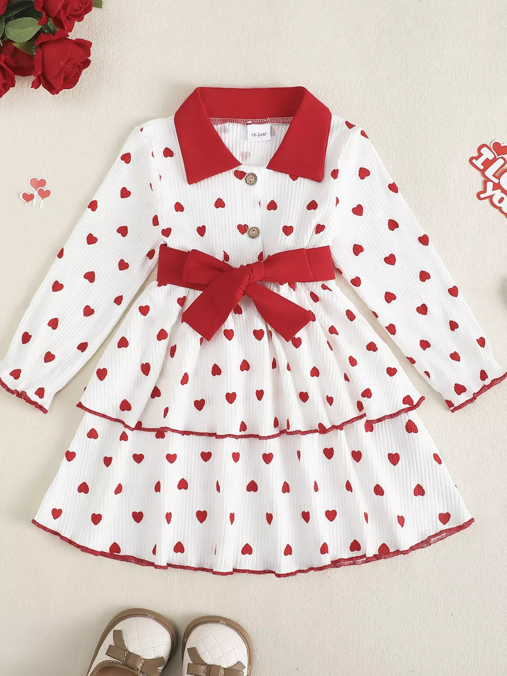 Baby girls white tiered dress with red hearts, red collar, red bow belt, and buttons.