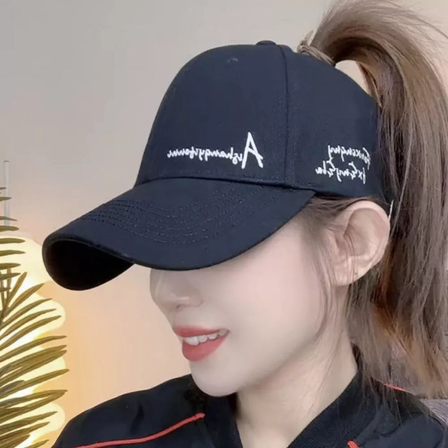 Black baseball cap with white embroidered logo and text, adjustable strap, ponytail opening